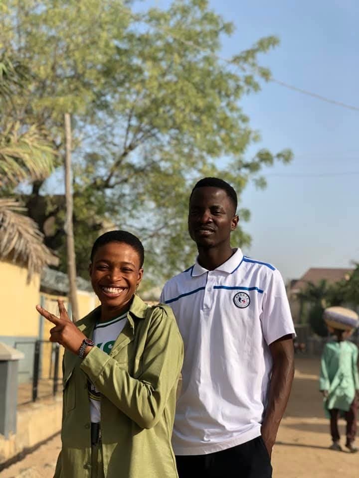 Scholarstica in NYSC service khaki uniform giving a peace sign with Joseph in white polo